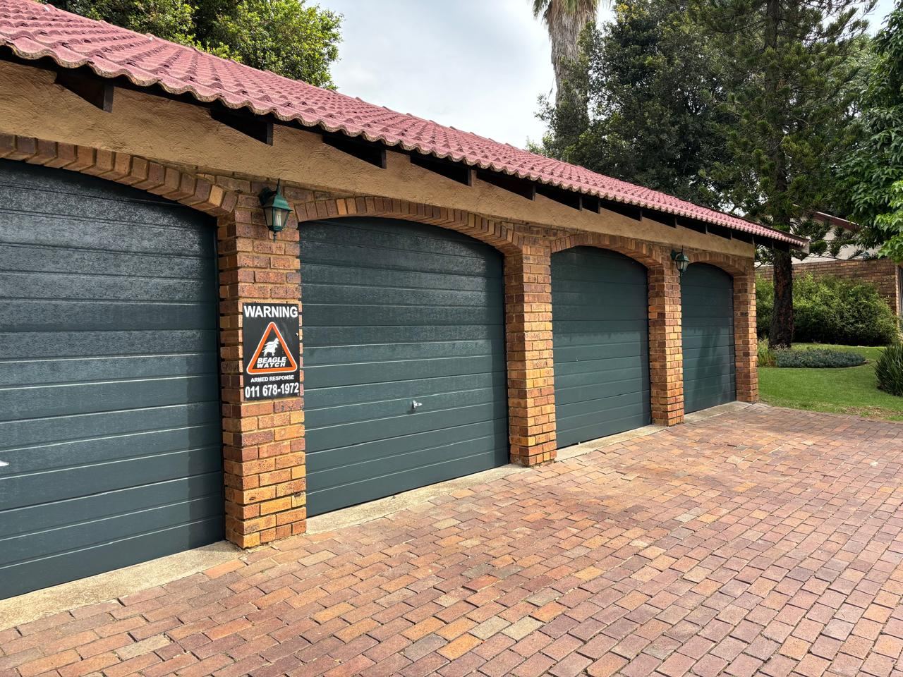 Row of finished dark green garage doors on a home with a tiled carport